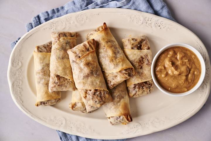 A plate of four vegetable egg rolls with a side of dipping sauce.