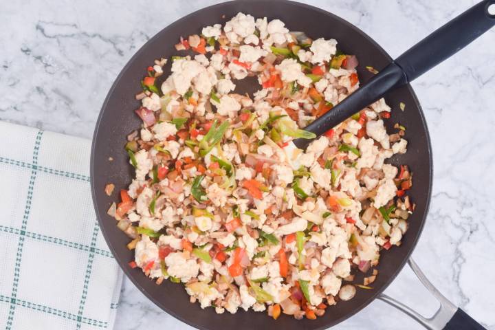 Filling for chicken wraps in a skillet including chicken, red peppers, mushrooms, garlic, ginger, and green onions.