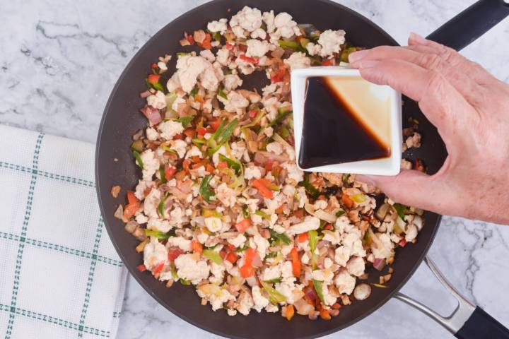 Hoisin and soy sauce being added to lettuce wrap filling in a pan.