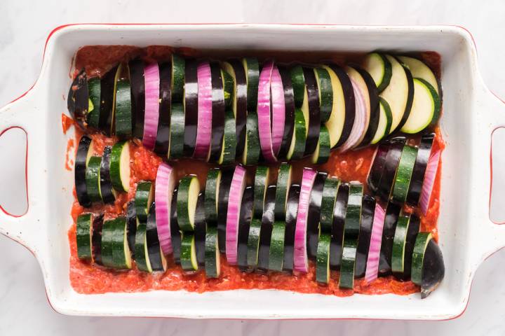 Zucchini and eggplant sliced and layered in a baking dish for ratatouille.