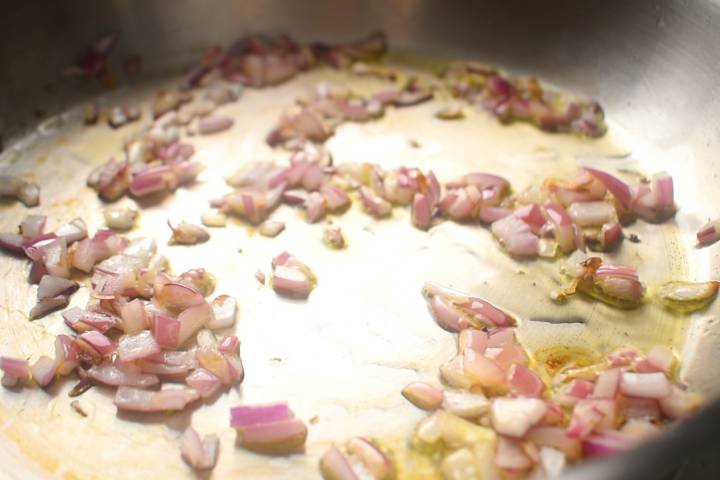 Red onions cooking in a skillet with oil.