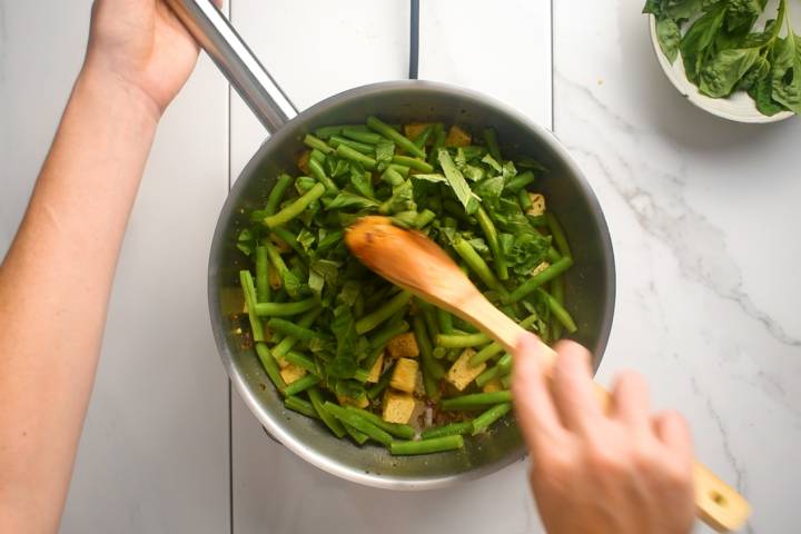Green beans being added to a skillet of tofu.
