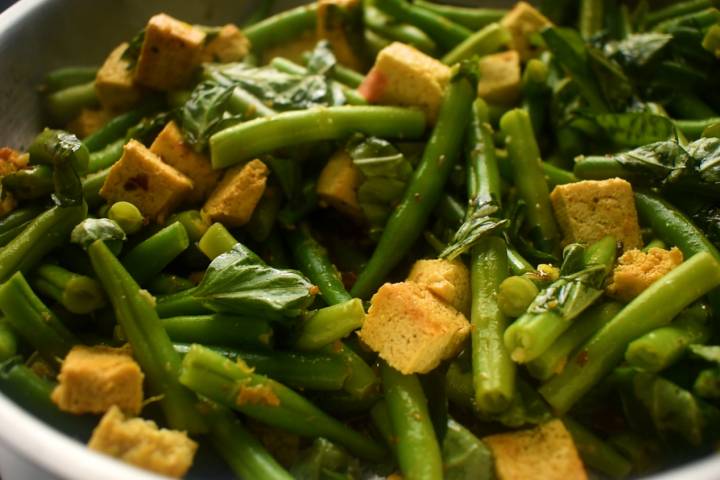 Basil and lemon juice being added to a skillet with tofu.