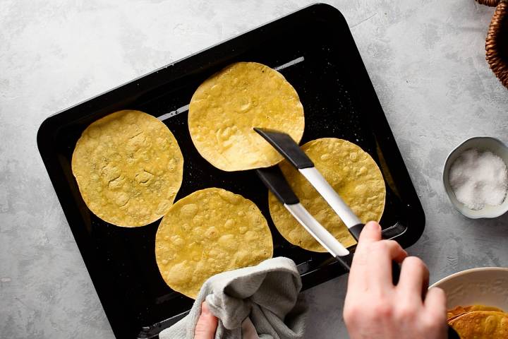 Corn tortillas being baked into tostada shells on a baking sheet. 