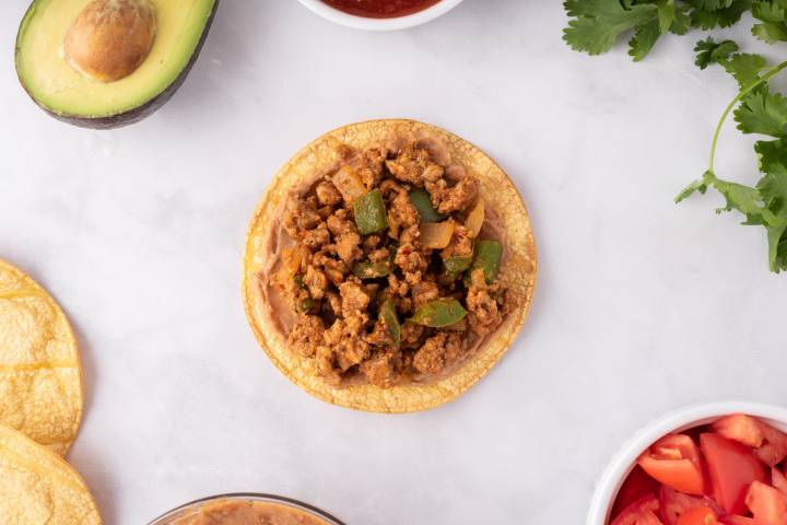 Ground turkey being added to a tostada shell.