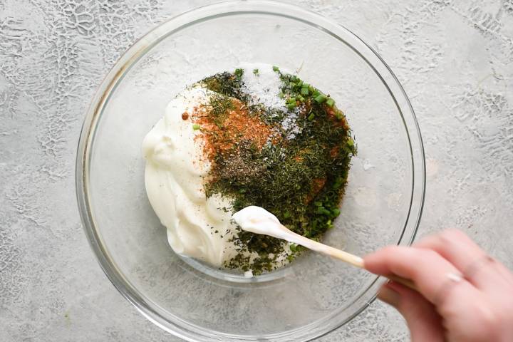 Greek yogurt, buttermilk, lemon juice, blackening seasoning, and dried herbs in a glass bowl.