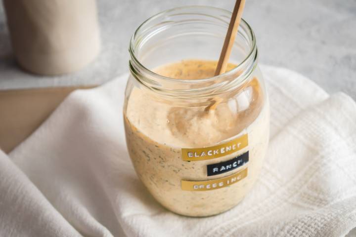 Greek yogurt blackened ranch dressing in a glass jar with a wooden spoon.