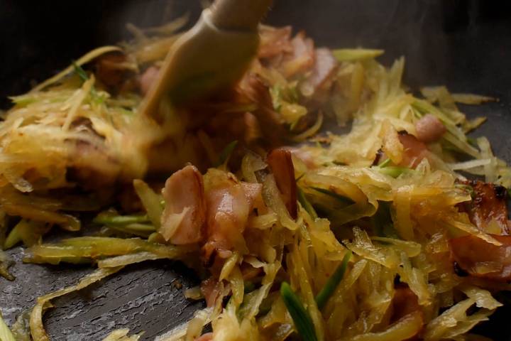 Hash browns, green onions, and turkey bacon cooking in a skillet.