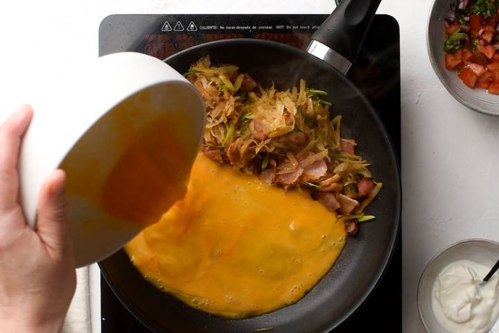 Eggs cooking with hash browns, green onions, and bacon for tacos.