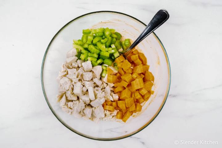 Cooked chicken, diced celery, and diced carrots in a bowl with buffalo dressing.