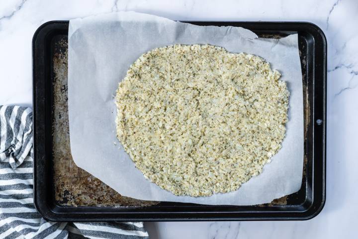 Raw cauliflower pizza dough on a baking sheet.