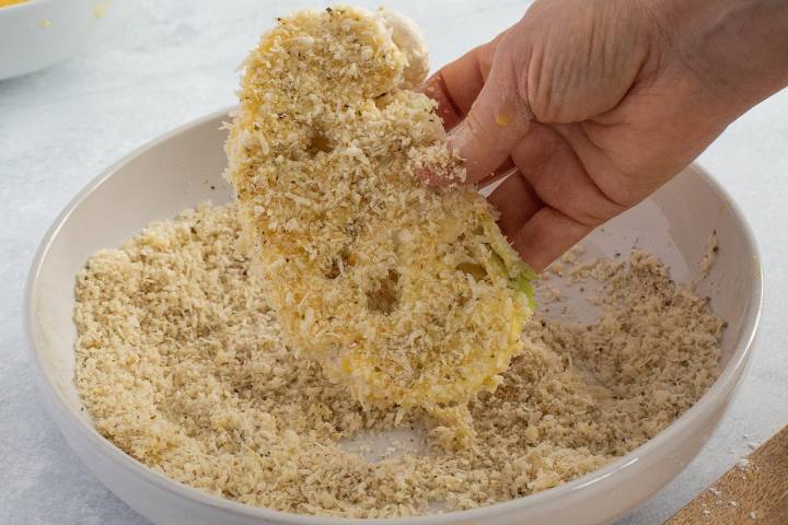 Cauliflower steaks being pressed into Panko breadcrumbs.