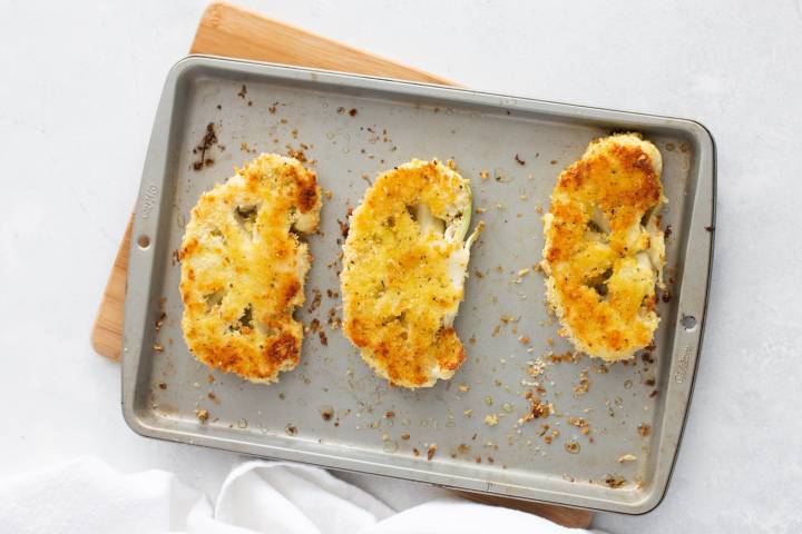 Crispy breaded baked cauliflower steaks on a baking sheet.