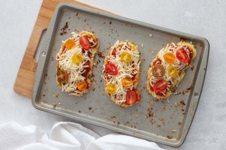 Cauliflower Parmesan on a baking sheet with shredded mozzarella and cherry tomatoes.