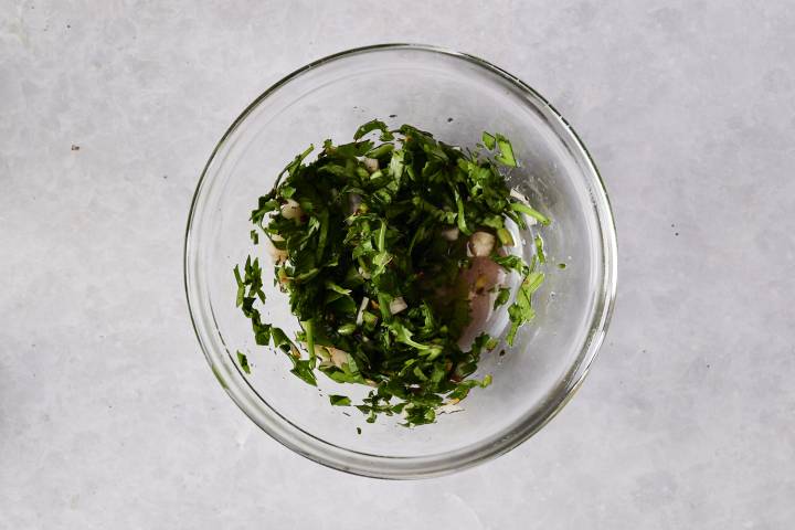 Glass bowl filled with freshly made chimichurri sauce with parsley, onions, and olive oil.