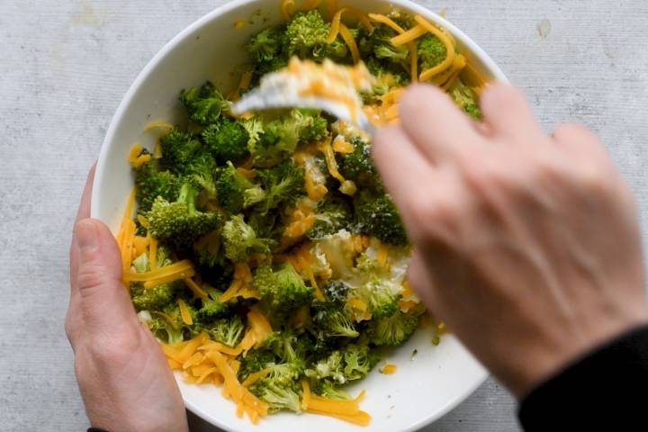 Broccoli, cheddar cheese, and cream cheese being stirred in a bowl.
