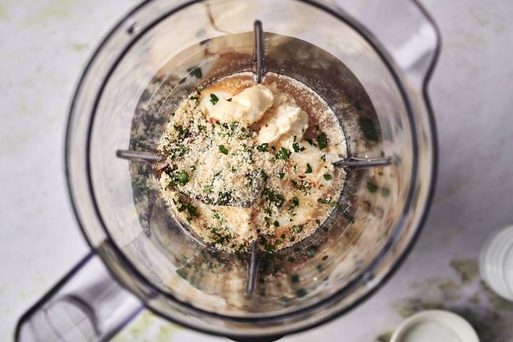 A blender filled with ingredients like mayonnaise, breadcrumbs, and chopped herbs, ready to be blended.