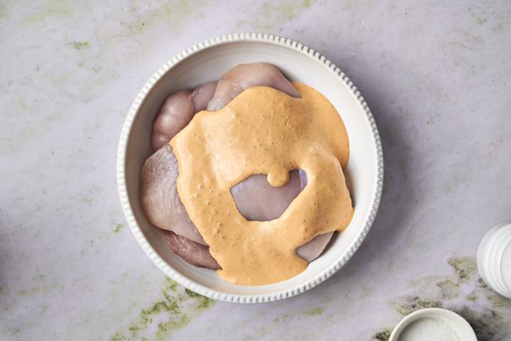 Chicken breasts coated with chipotle ranch sauce in a white bowl, ready for marinating.
