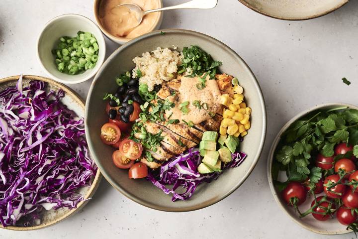A Chipotle Ranch Chicken Bowl with grilled chicken, quinoa, black beans, cherry tomatoes, corn, avocado, purple cabbage, green onions, cilantro, and a side of chipotle ranch sauce.