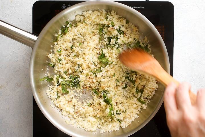Cilantro and lime juice being added to cauliflower rice in a skillet.