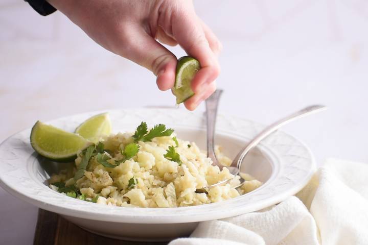Lime juice being squeezed over a bowl of cauliflower rice.