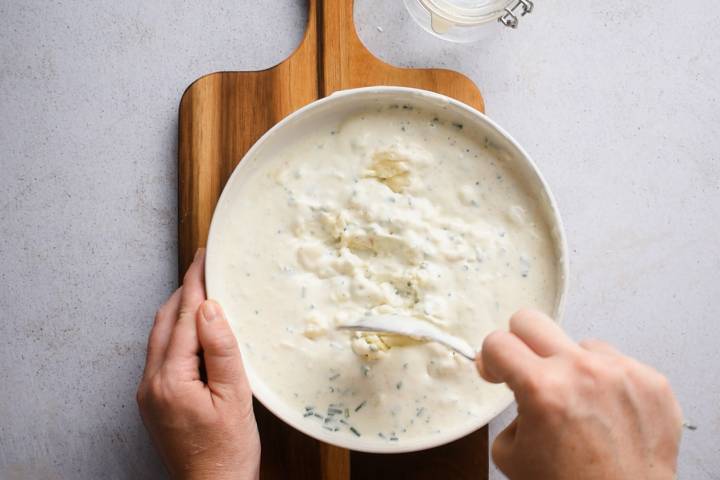 Greek yogurt, gorgonzola cheese, chives, buttermilk, and vinegar being stirred in a bowl.