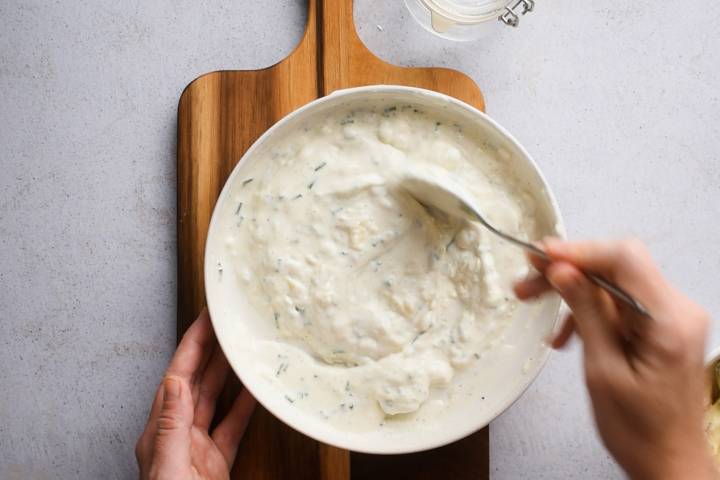 Gorgonzola dressing with Greek yogurt being stirred in a white bowl.