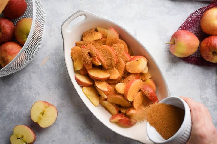 Sliced apples being tossed with cinnamon, sugar, cornstarch, lemon juice, and nutmeg in a baking dish.