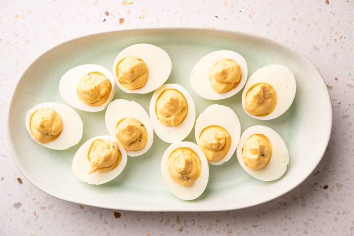 Plate of deviled eggs with creamy, yellow filling, arranged neatly on a light green platter.