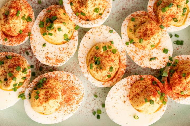 Deviled eggs sprinkled with paprika and garnished with chopped chives on a light green surface. The eggs are halved, showcasing creamy yolk filling.