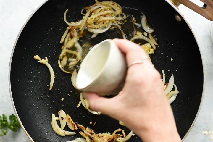 White wine being poured into a skillet with onions.