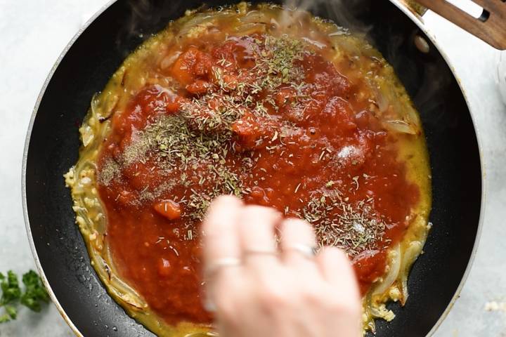 Tomatoes, herbs, and sliced onions in a skillet for sauce.