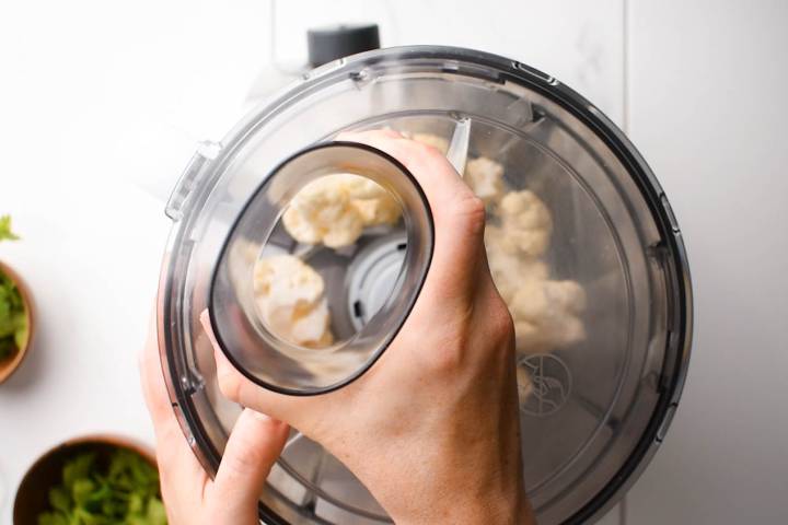 Cauliflower being added to a food processor to make rice.