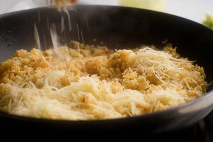 Parmesan cheese being sprinkled on a skillet with garlic cauliflower rice.