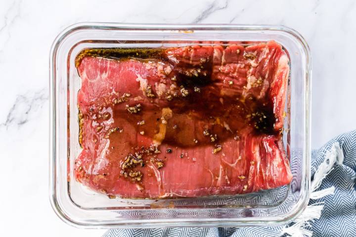 Raw flank steak in a glass container with balsamic marinade.