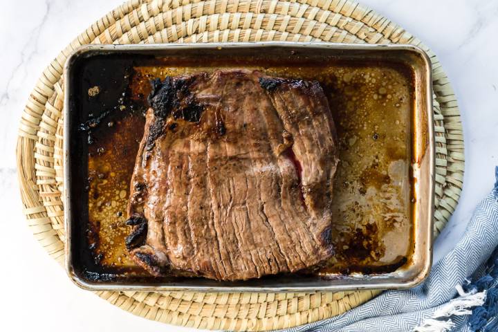 Broiled flank steak with balsamic marinade on a baking sheet.