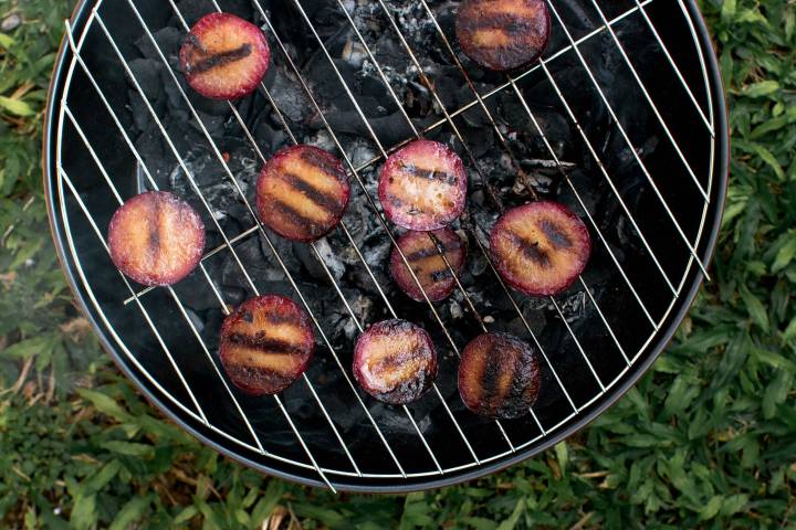 Plums being grilled on a small outdoor grill.