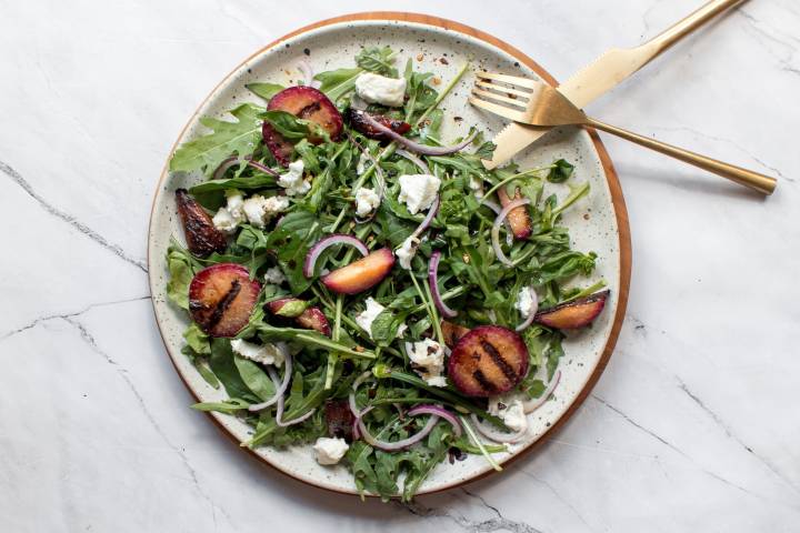 Grilled plum salad on a plate with goat cheese, arugula, and red onions. 