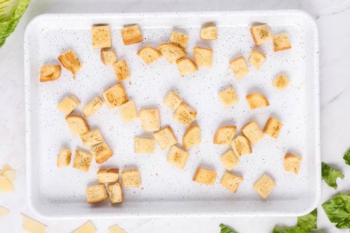 Homemade croutons on a baking sheet with salt and pepper.