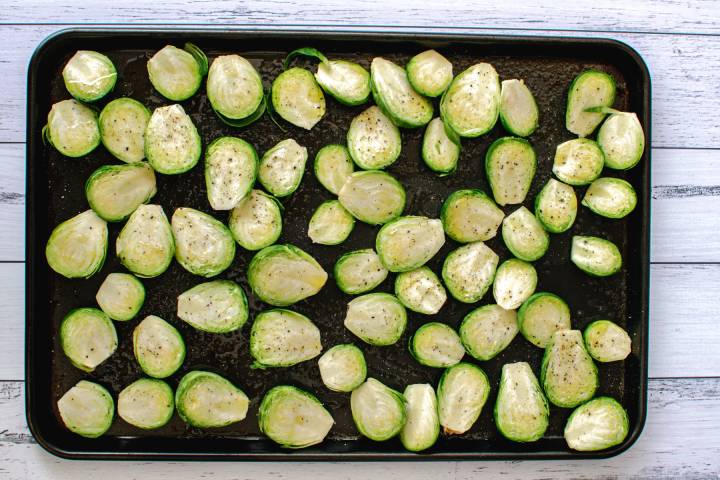 Raw, halved Brussels sprouts on a baking sheet with olive oil, salt, and pepper.