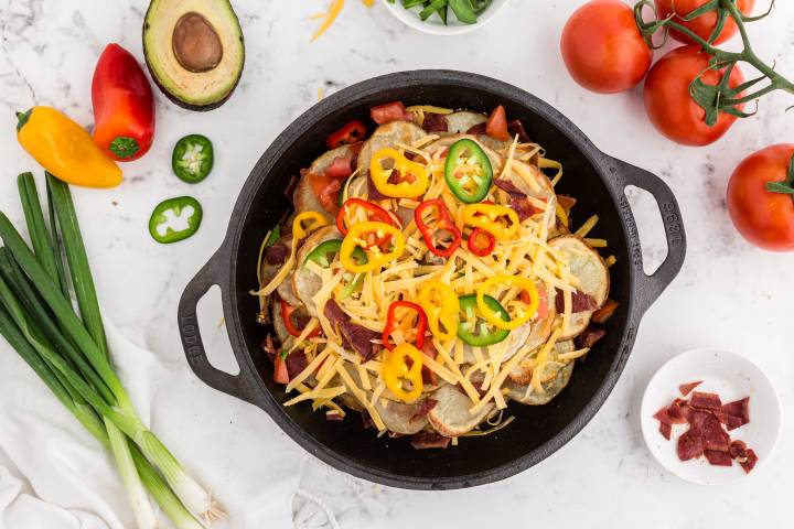 Irish nachos in a skillet with layers of potato chips, cheese, peppers, and green onions.
