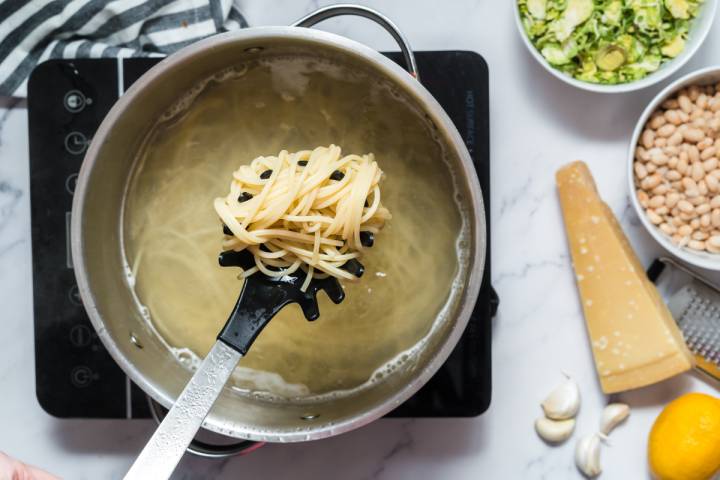 Pasta cooking in a pot and being lifted on a slotted spoon.