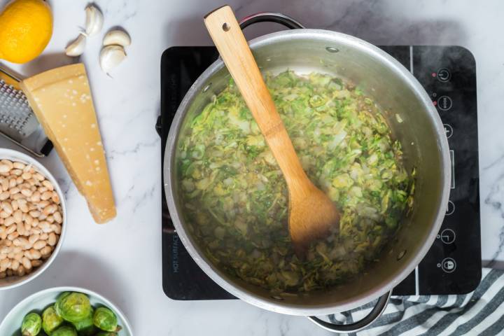 Brussel sprouts cooking in a large pot with garlic, onions, and spices.