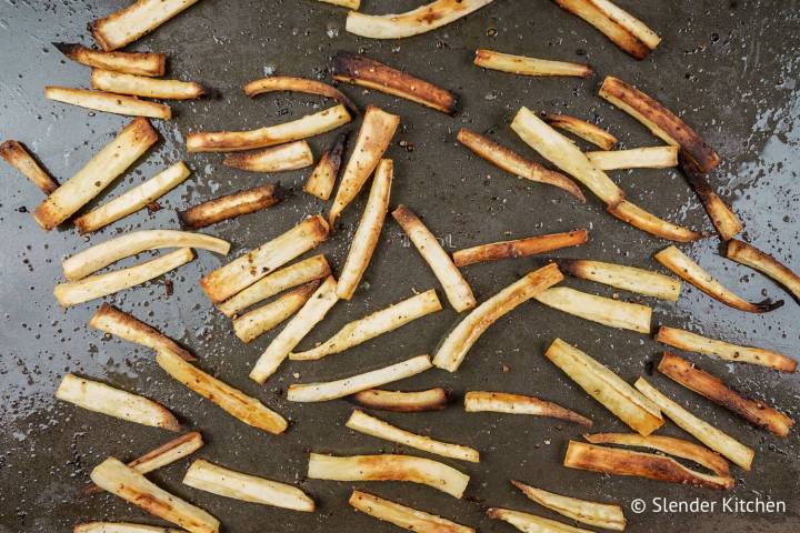 Roasted parsnip fries on a baking sheet that are browned and crispy.