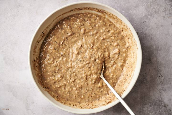 A top-down shot of a person adding peanut butter to a jar of overnight oatmeal.