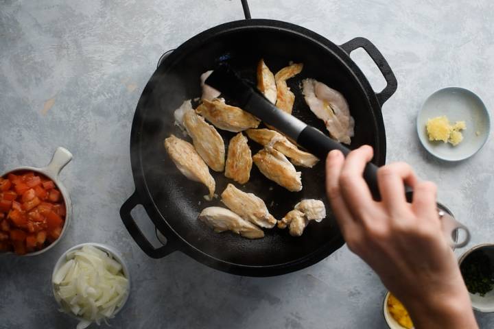 Chicken breast strips cooking in a cast iron skillet.