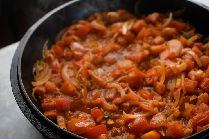 Ranchero sauce being simmered in a skillet with tomatoes, onions, garlic, and jalapeno peppers.