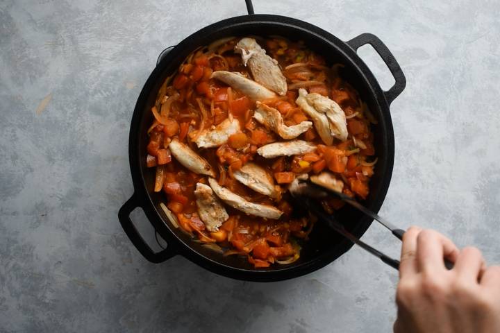 Chicken breast being nestled into ranchero sauce in a skillet.
