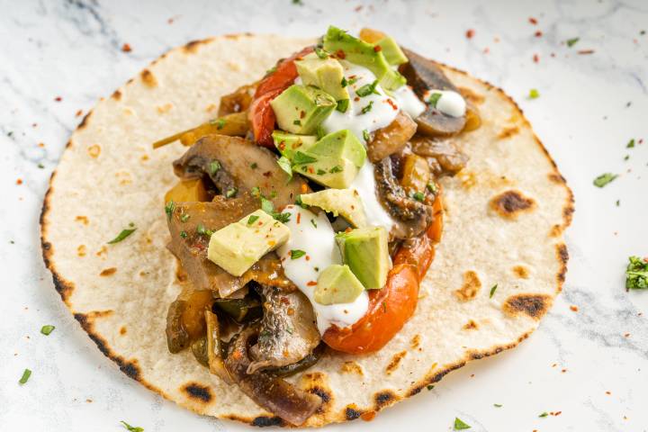Mushroom fajitas with guacamole and sour cream on a flour tortilla.