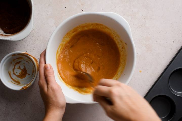 Pumpkin, eggs, almond butter, and maple syrup being stirred in a bowl.